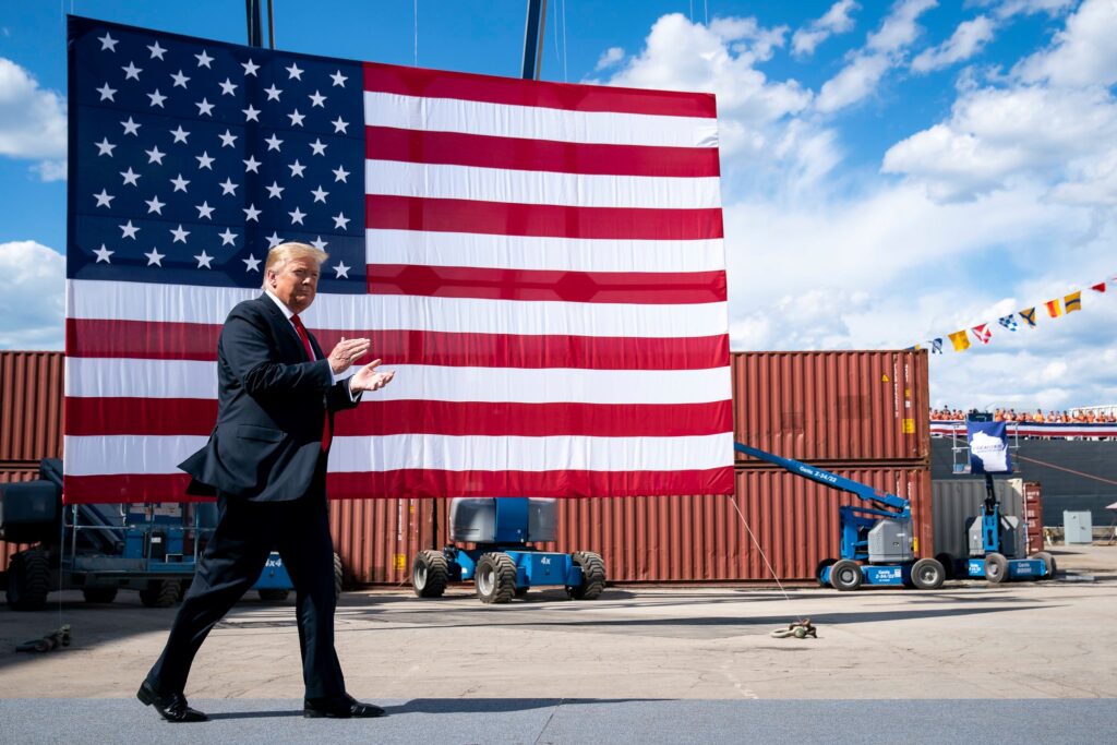 Donald Trump walks in front of a large American flag.